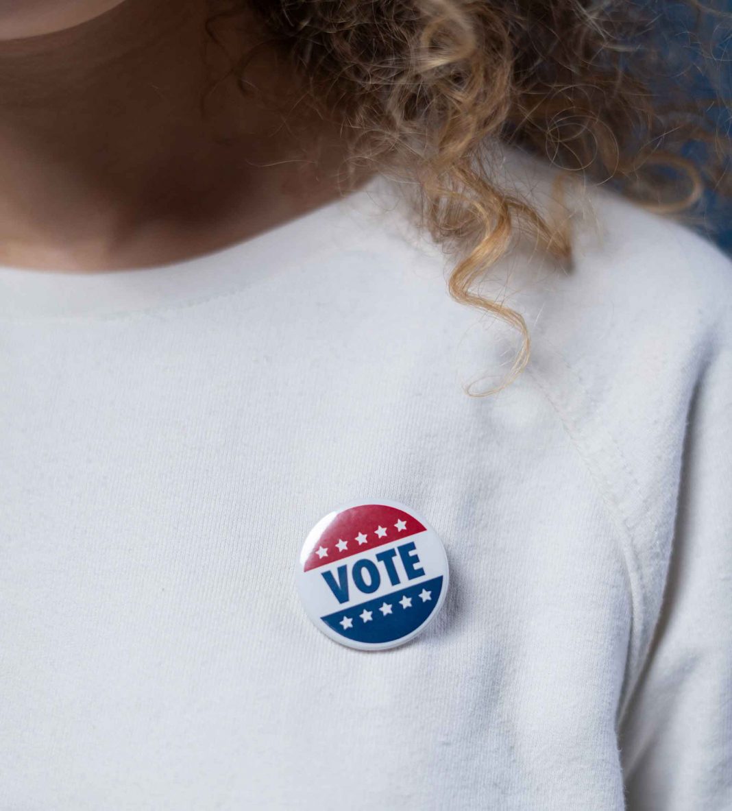 vote button on woman wearing white sweatshirt, with curly hair